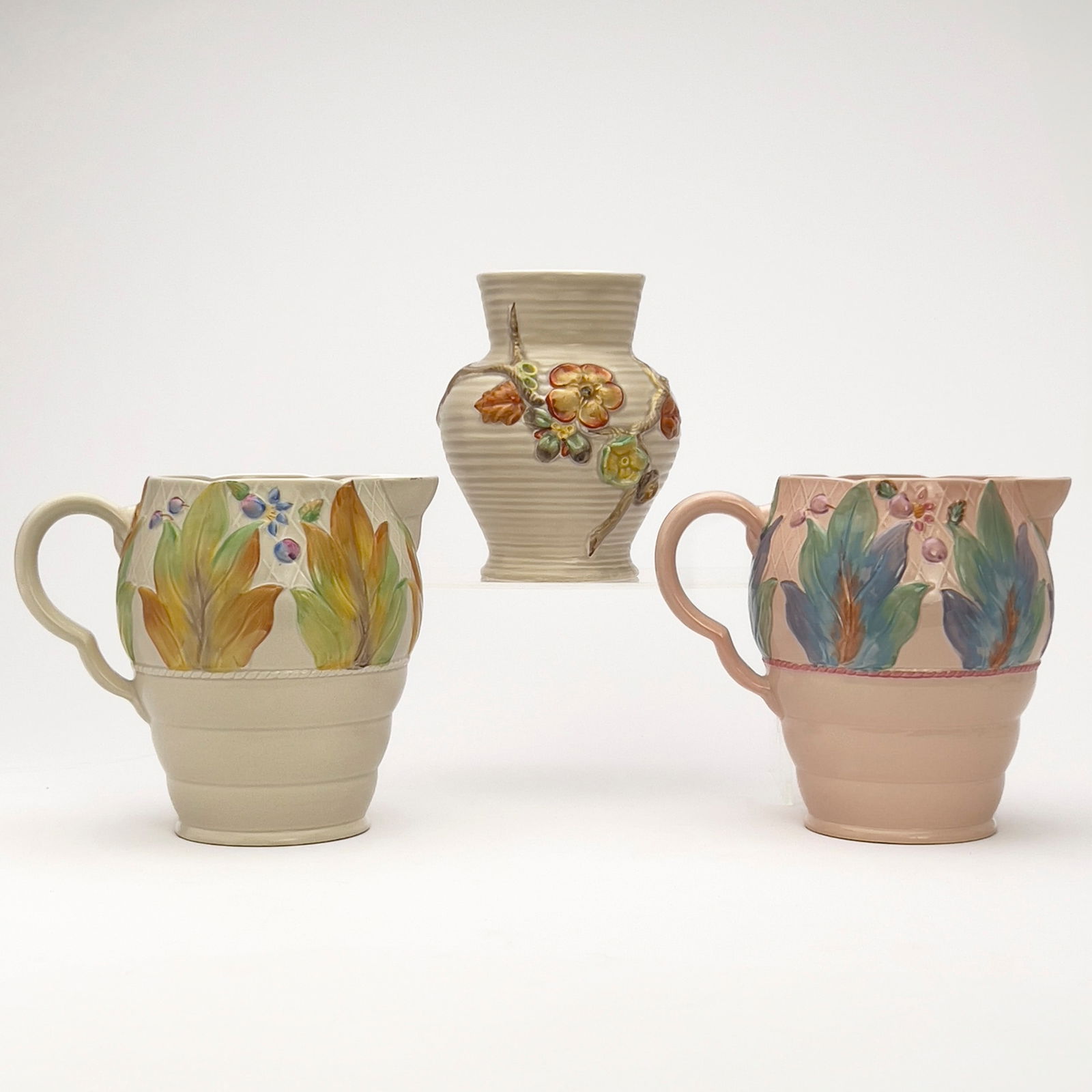 Clarice Cliff - Newport Pottery Ceramic Vessels, Group of 3: Lot 81 Clarice Cliff English (1899-1972) Newport Pottery Ceramic Vessels, Group of 3 hand-painted ceramic Comprising of two jugs with an enameled leaf and berry relief in pink and cream and a ribbed v