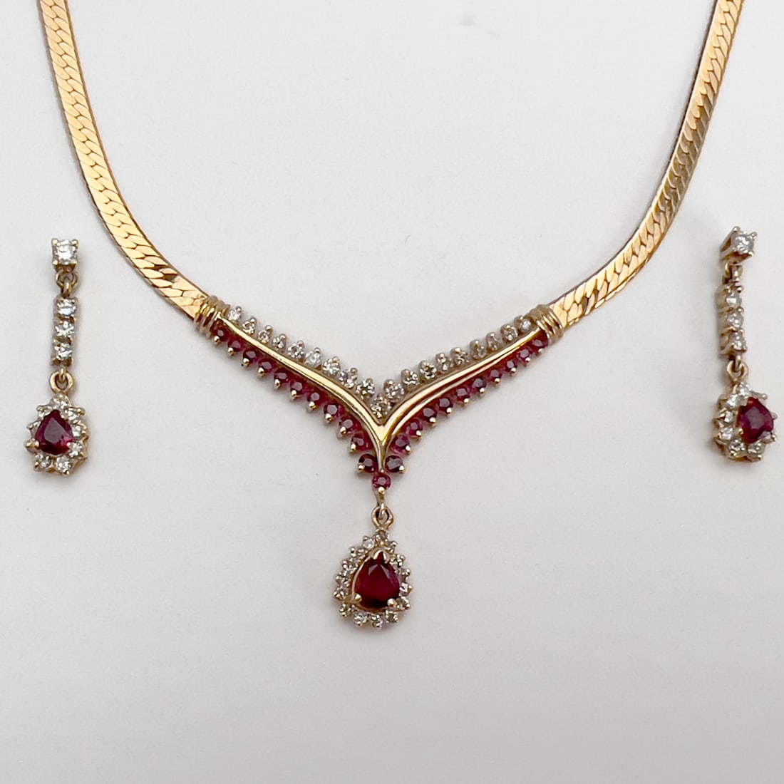 Gold and Ruby Necklace and Drop Earring Set: Lot 34 Gold and Ruby Necklace and Drop Earring Set 14k gold, diamond, ruby A 14k yellow gold herringbone link necklace set with 19 diamonds and 23 rubies in a V formation with a pear-cut .5 ct ruby p