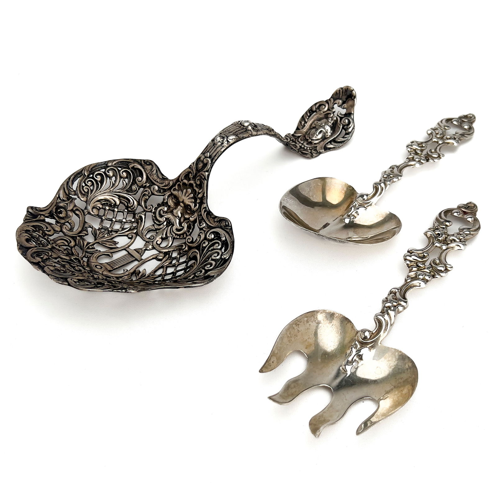 Three Large Ornate Silver Serving Pieces: Lot 172 Three Large Ornate Silver Serving Pieces sterling silver Sterling silver group, comprising of one large reticulated serving spoon, and a serving set with ornate carved handles total