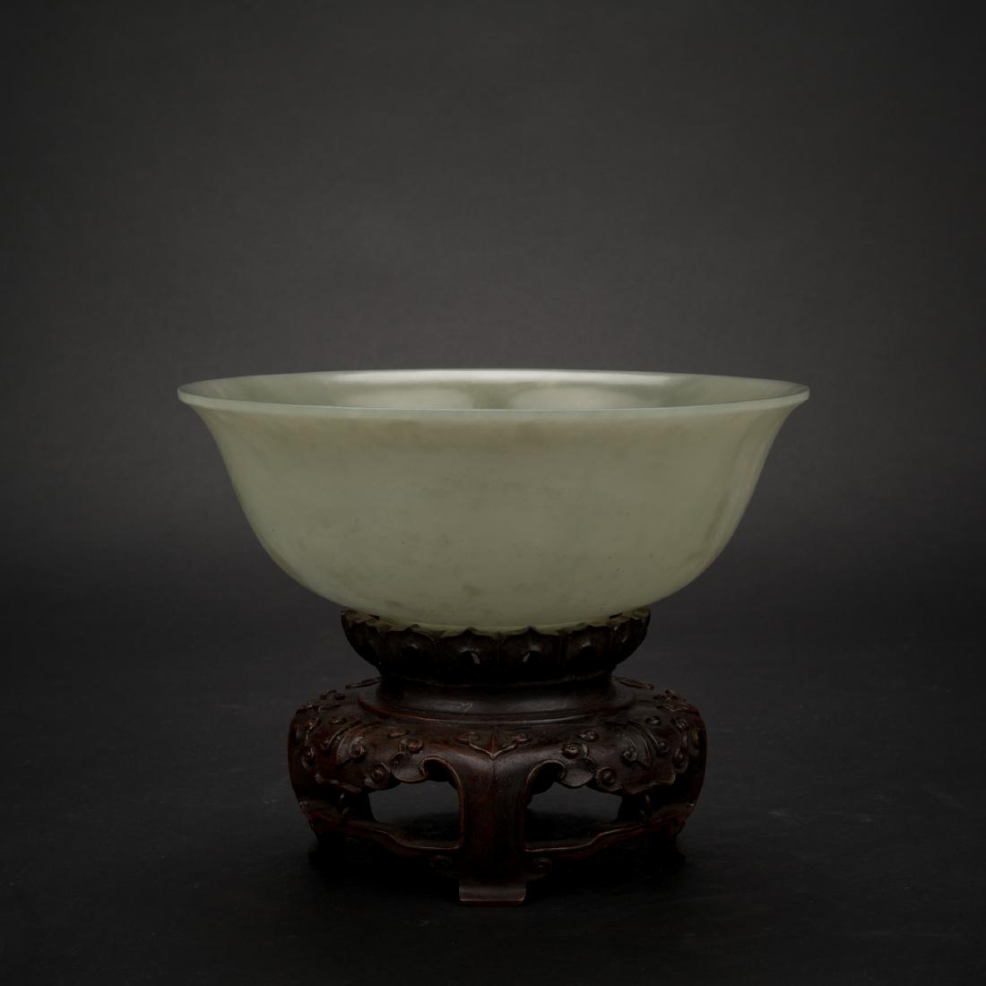 FINE JADE BOWL ON STAND: The deep bowl body further to slightly flared rim. Displayed upon a carved hardwood base. The carving is smooth, displayed pale-celadon iridescent, finely polished clean tone, with moist milky appeara