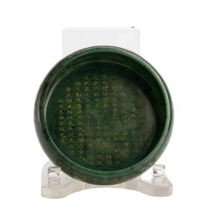 GREEN JADE & GILT INSCRIBED PLATE: Measurements: Length: 17cm, width: 17cm, Height: 5.5cm Of round shape, raised on short circle feet, inscribed imperial poem at the exterior, the stone is of spinach green tone with black veins.