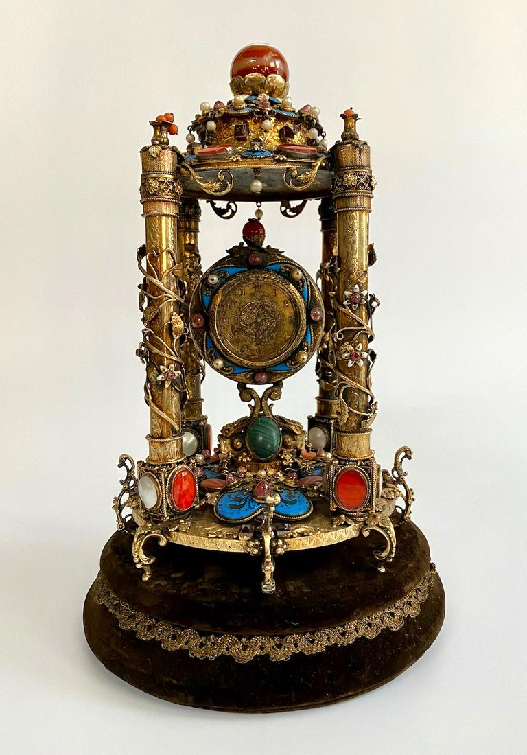 AN AUSTRO-HUNGARIAN SILVER, ENAMEL AND: AN AUSTRO-HUNGARIAN SILVER, ENAMEL AND CALCEDONY-MOUNTED TABLE CLOCK, An Austro Hungarian Gilt Silver, Enamel & Semi Precious Stone Table Clock Circa 1940 or earlier Highly decorated with foliage surr