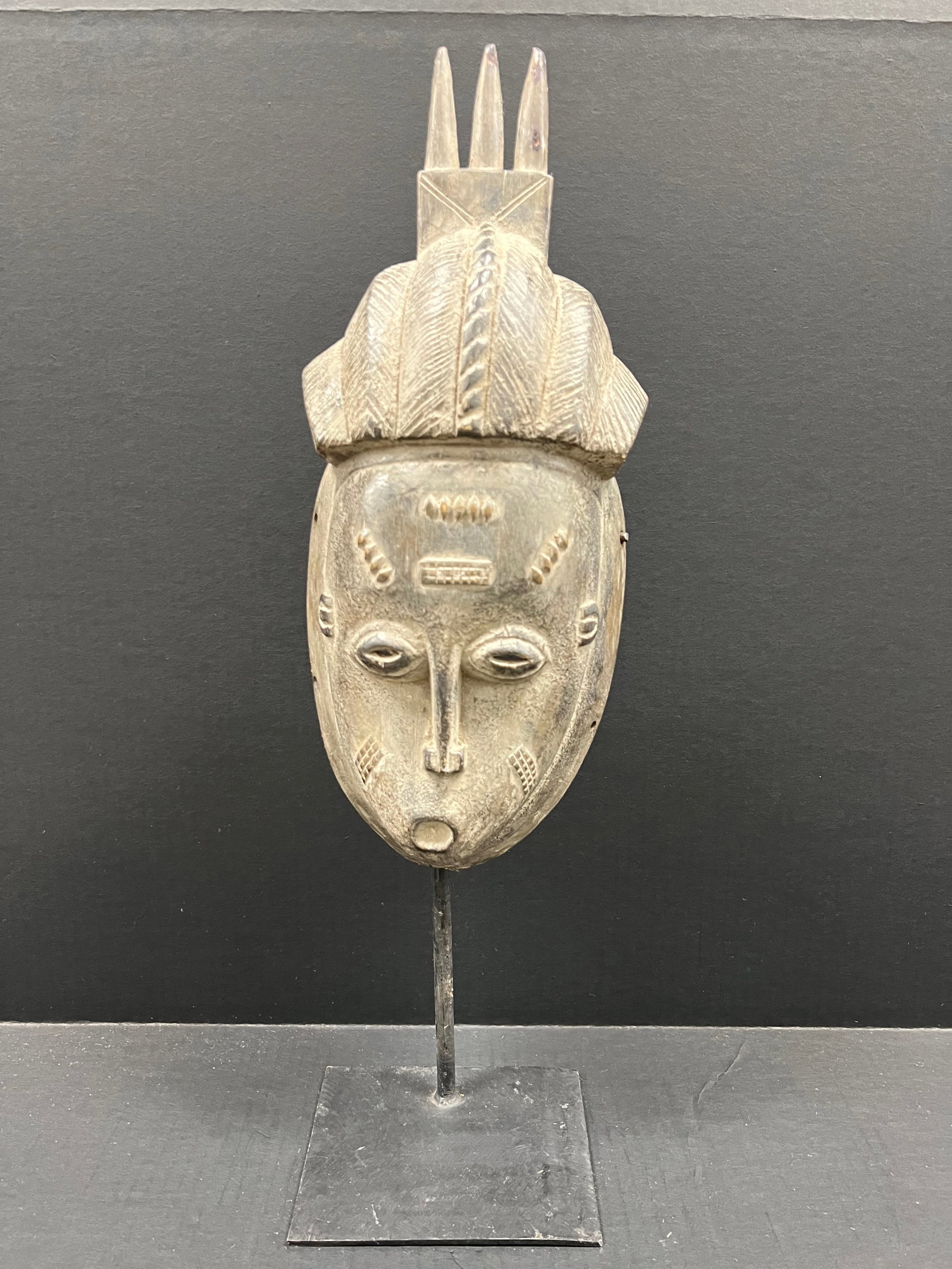 Carved Wood Baule Mask with Display Stand: African Tribal Art Carved Wood Baule Mask with Display Stand. The dimension is 22 inches high x 7 inches wide. Please be aware that some of the items are vintage, secondhand, old ages, antiques and