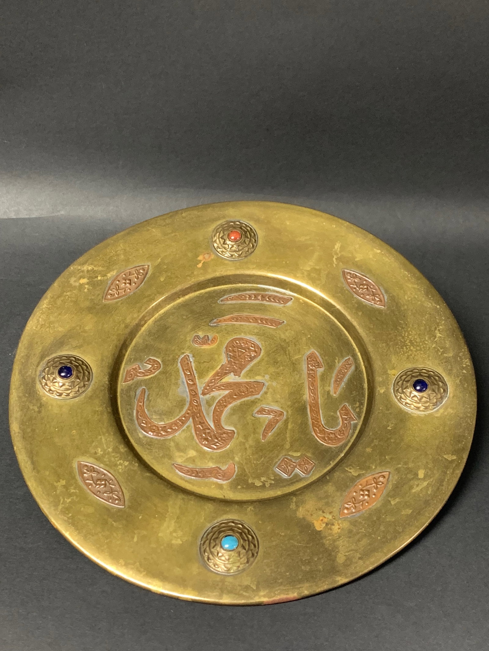 Vintage Middle Eastern Brass Plate with Arabic Calligraphy and Gemstone Inlays: Vintage Middle Eastern Brass Plate with Arabic Calligraphy and Gemstone Inlays. The dimension is 8.75 inches high x 8.75 inches . Please be aware that some of the items are vintage, secondhand, old ag