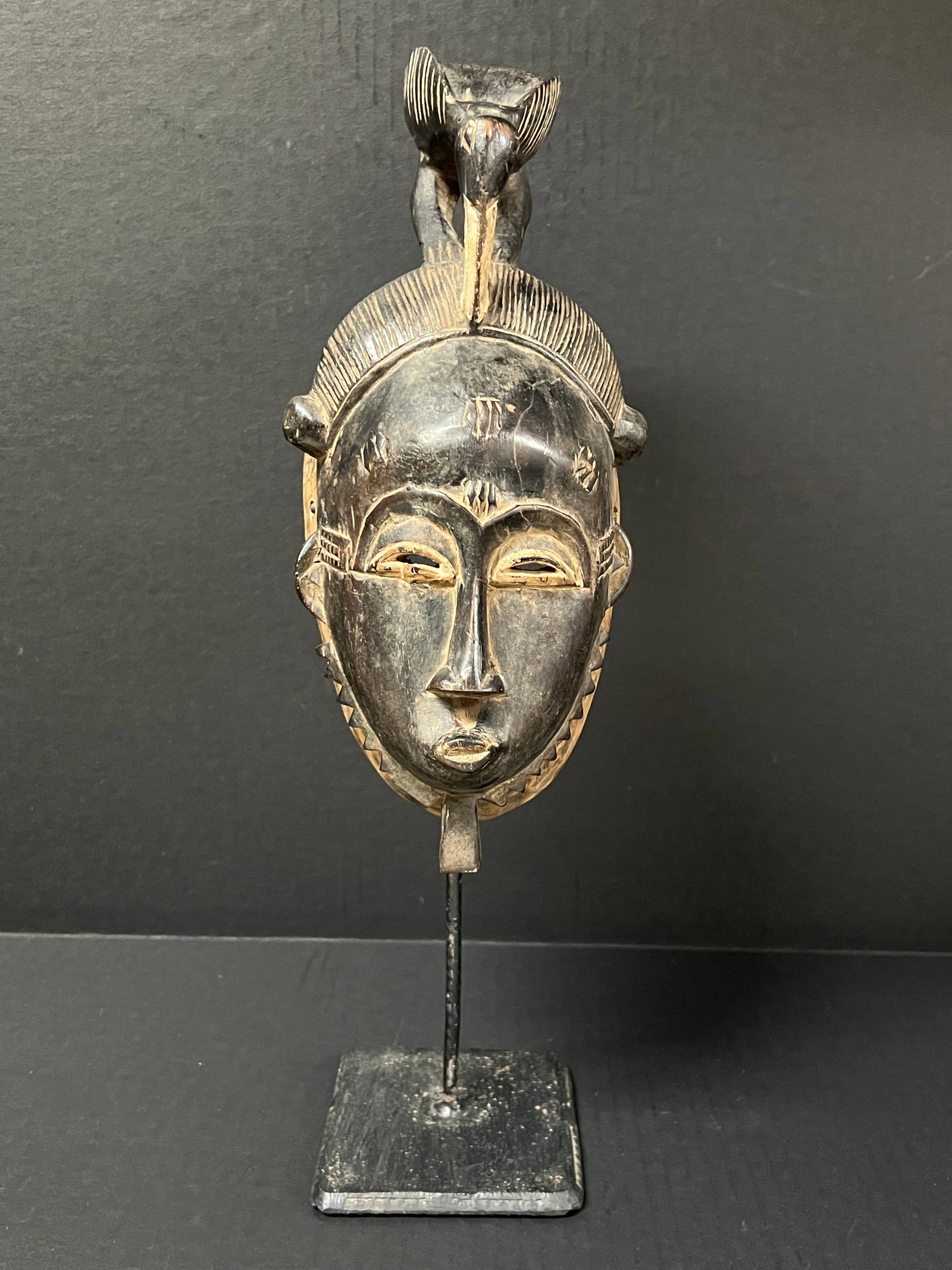 Carved Wood Baule Mask With Display Stand: African Tribal Art Carved Wood Baule Mask with Display Stand. The dimension is 12 inches high x 5 inches wide. Please be aware that some of the items are vintage, secondhand, old ages, antiques and ma