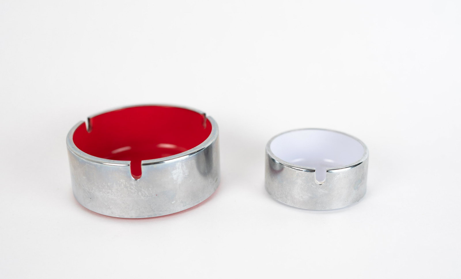 Set of 2 Isamu Kenmochi Chrome and Plastic Ashtrays in Pinkish Red, White: Set of 3 chrome and plastic ashtrays in sizes small and medium, which nest together. Stamped underneath with makers information; medium is marked patent pending (design attrb to Isamu Kenmochi), while