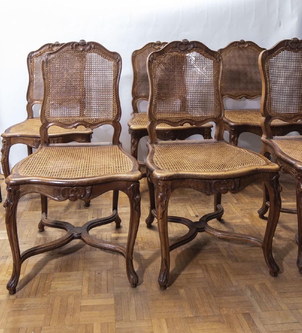 Six chaises cannées en bois naturel mouluré et sculpté : Six chaises cannées en bois naturel mouluré et sculpté - Le dossier plat à décors sculpté de fleurs - Pose sur des pieds galbés à enroulement réunis par une entretoise en X - Style Louis XV -
