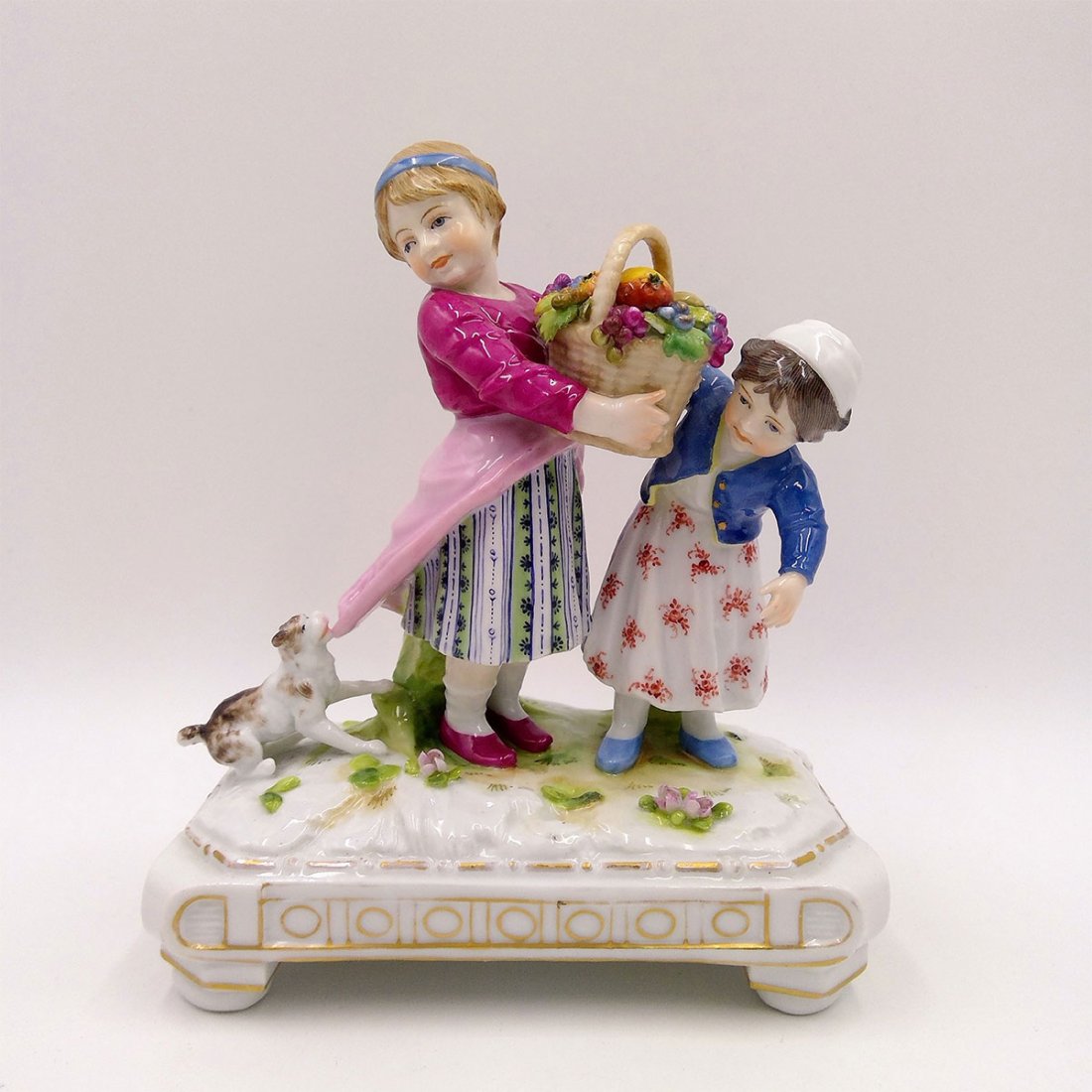 KARL ENS GERMAN PORCELAIN GROUP FIGURINE GIRLS: Volkstedt Rudolstadt Karl Ens Figurine of Two Girls Carrying a Basket of Fruit and a Dog Pulling Girl's Dress. Circa 1900-1910.