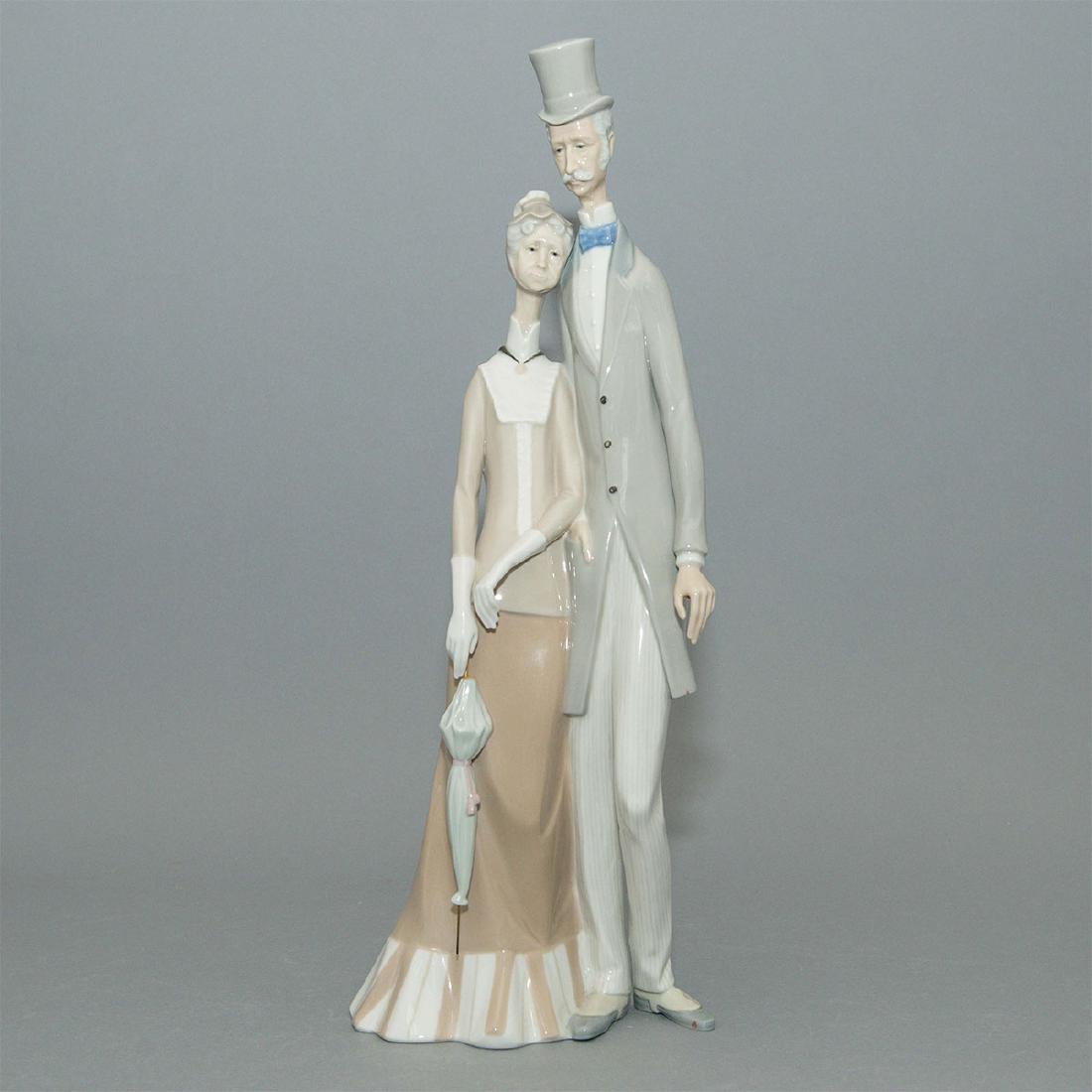 LLADRO OLD FOLKS PORCELAIN FIGURINE 1033: The Lladro double figurine Old Folks, Number 1033. It depicts a venerable Edwardian man and woman taking a stroll. The man wears a top hat, morning coat, pinstriped trousers, and shoes with spats, whi