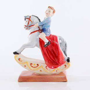 ROYAL DOULTON THE ROCKING HORSE HN2072 FIGURINE: A Royal Doulton figurine designed by Leslie Harradine and issued from 1951 to 1953. Decorated in a blue, red and yellow colorway, it is modeled as a young boy sitting atop his rocking horse, with an