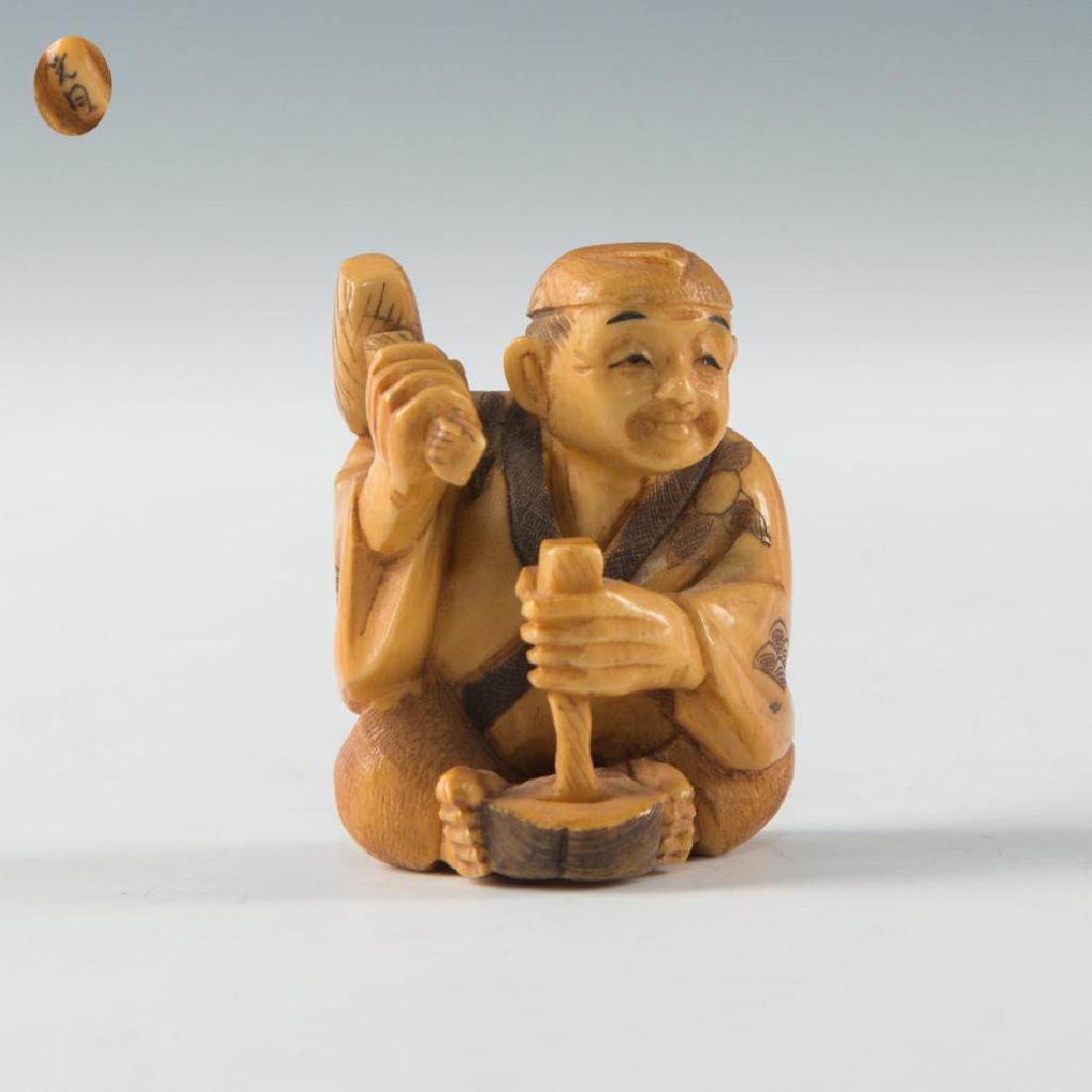 ANTIQUE JAPANESE CARVED BONE NETSUKE OKAME MASK MAKER: Netsuke carving of a mask maker. Unusual figure depicting a man holding Okame mask between his feet. Signed on the foot. Dimensions: 1.5"H Country of Origin: Japan
