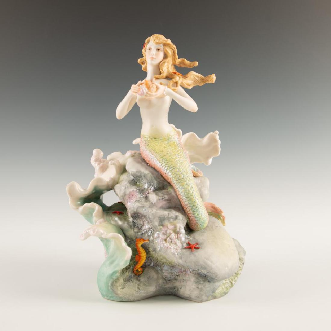 CYBIS LARGE PORCELAIN FIGURINE SEA NYMPH MERMAID: Sculpture of a semi nude Sharmine sitting on rocks with sea shell Signed on the back. Model number 269. Dimensions: 13"H x 8"W Issued: Circa 1978-1982 Country of Origin: USA