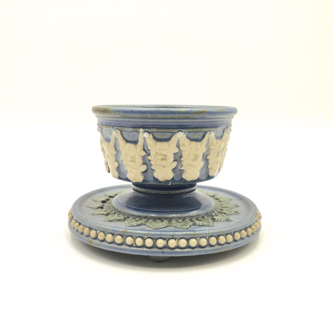 VICTORIAN-ERA BLUE APPLIED RELIEF DOULTON OPEN SALT: 1881 Lambeth artware, pale glazed with green, white slip relief. Dated on the bottom with rosette logo, and several artist marks abound. This unique, footed, and saucered open salt features a rare azu