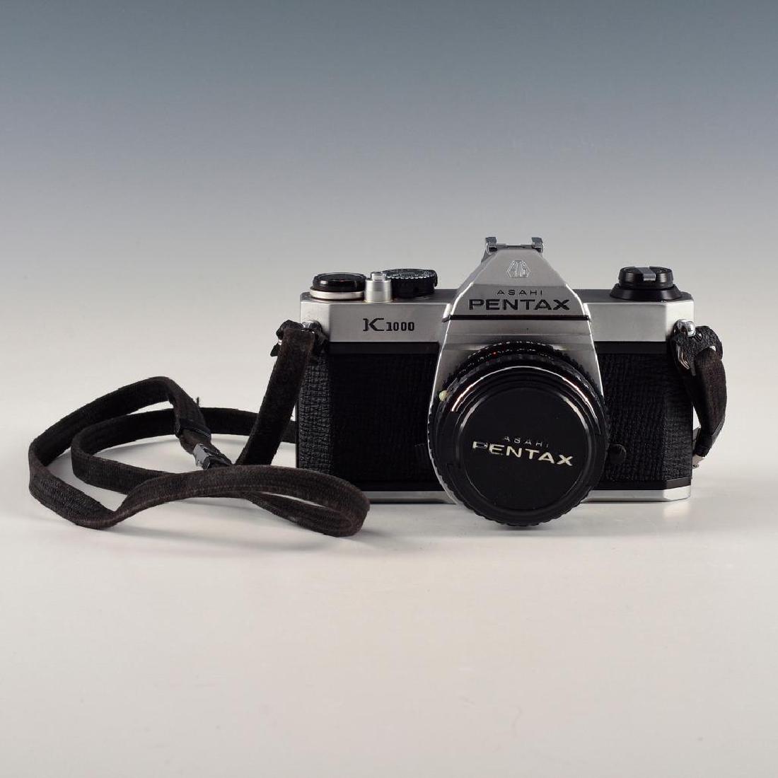 ASHAI PENTAX K1000 VINTAGE SLR CAMERA WITH STRAP, LENS: Ashai 2 F50mm lens on metered reflex 35mm camera from Pentax. Issued: 1976-1997 Dimensions: 5"L X 3.5"D X 4"H Edition Number: 6080537 Manufacturer: Pentax Country of Origin: Japan