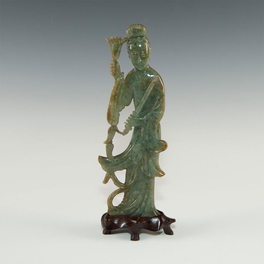 CARVED JADEITE GUANYIN FIGURAL STUDY ON WOOD STAND: Natural carved jade with green and russet inclusions. On wooden base. Issued: 19th century or earlier Dimensions: 10"H with base Country of Origin: China