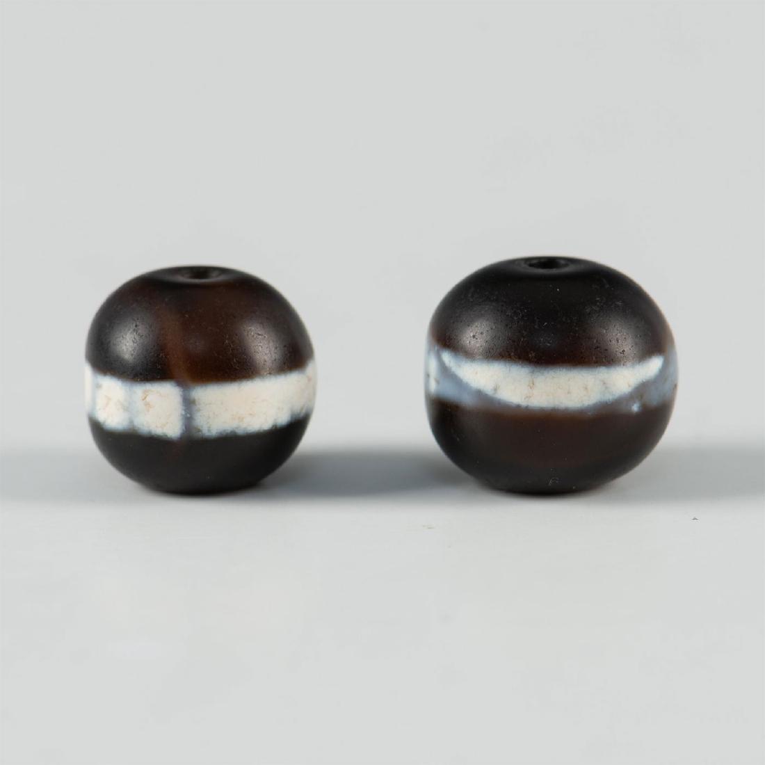 LOT OF TWO TIBETAN DZI BEADS: Traditional Tibetan dzi beads, each with bluish white bands in center. Issued: 19th-20th c. Dimensions: 0.5"D largest Provenance: Acquired in Nepal in the 1960's Country of Origin: Tibetan