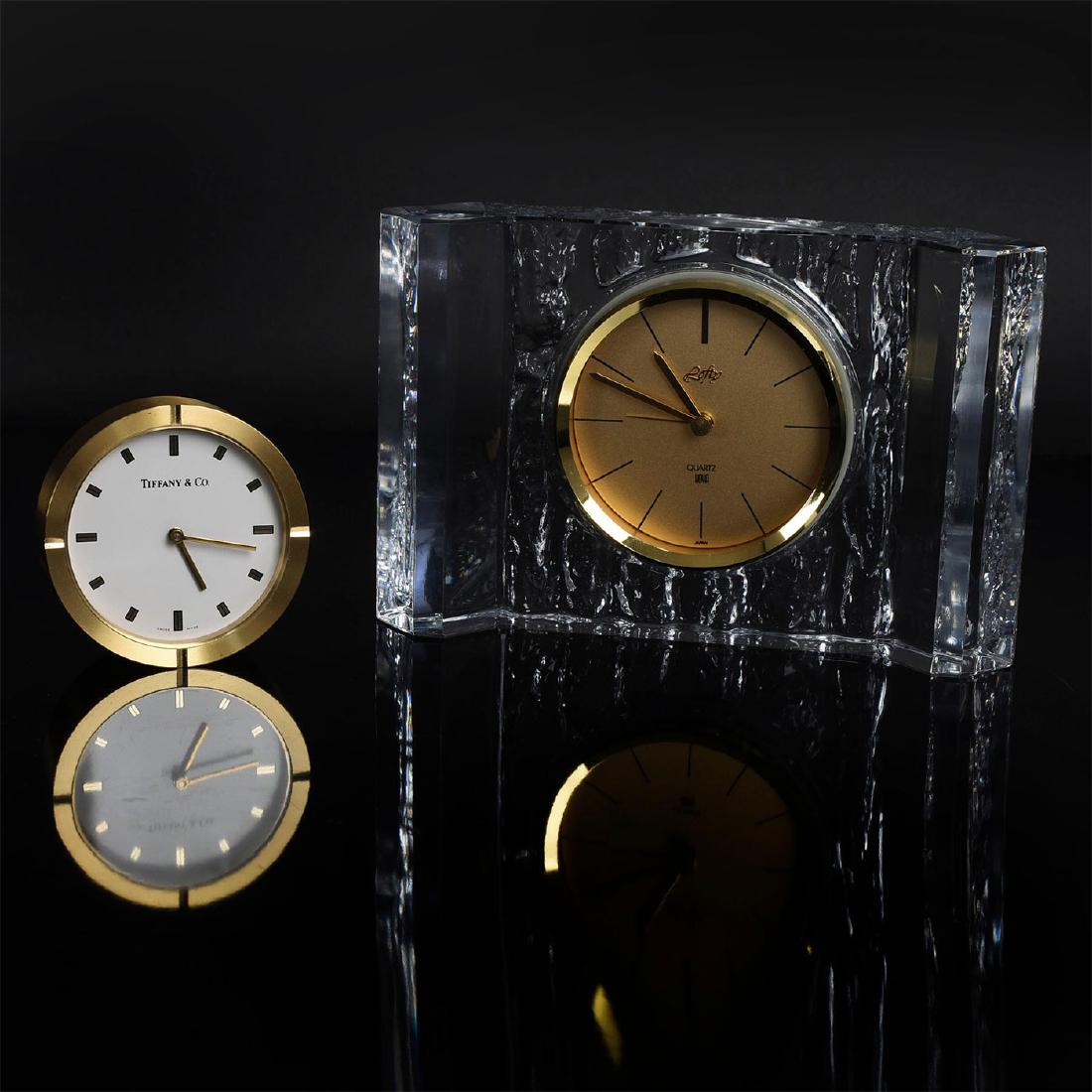 GROUP OF TWO CLOCKS, ONE TIFFANY & CO.: Two stylish analog desk or table clocks. One small round desk clock, marked to face TIFFANY & CO., and SWISS MADE. Second clock presented in heavy glass crystal base, marked to face LOFY, and QUARTZ H