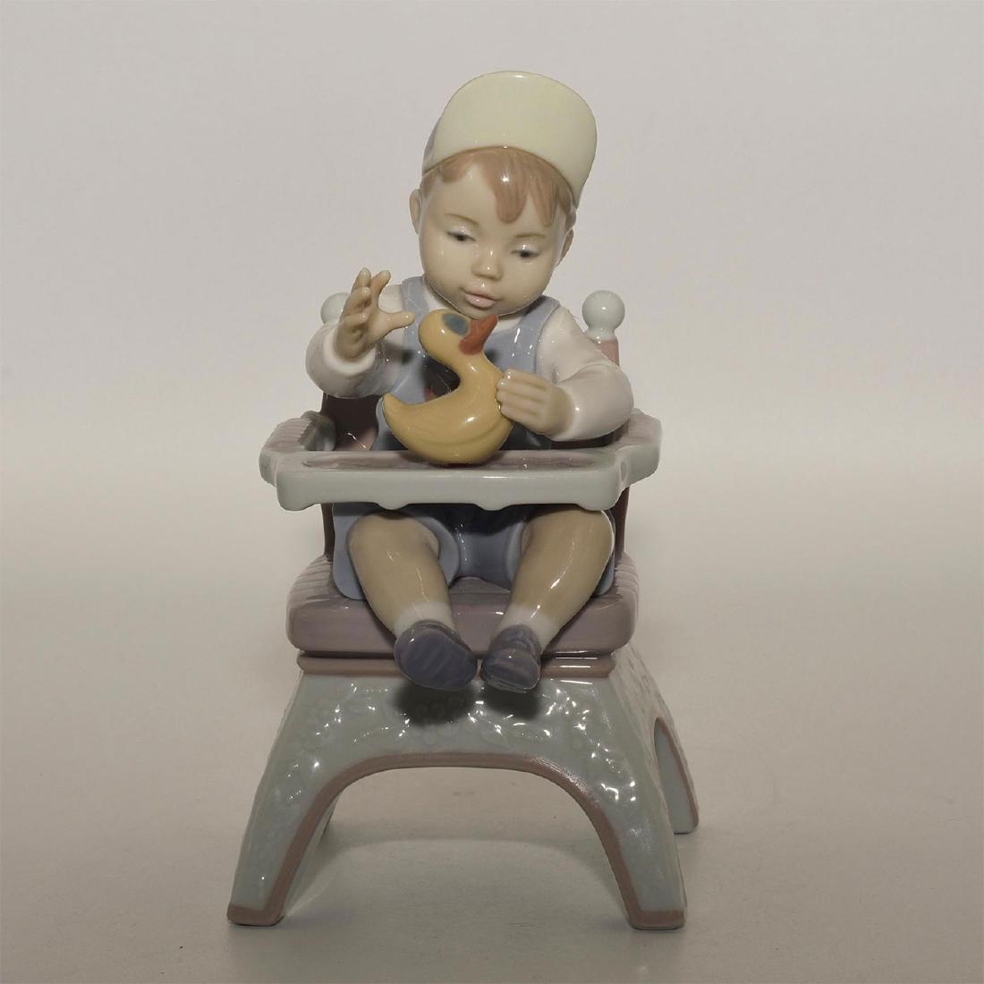 LLADRO FIGURINE RUBBER DUCKY: Boy sitting on a baby chair with a duck on the table - Lladro number 01006300. JUGANDO CON EL PATITO (with box). Artist: Jose Coderch Issued: 1996 Dimensions: 9.01"H Manufacturer: Lladro Country of Or