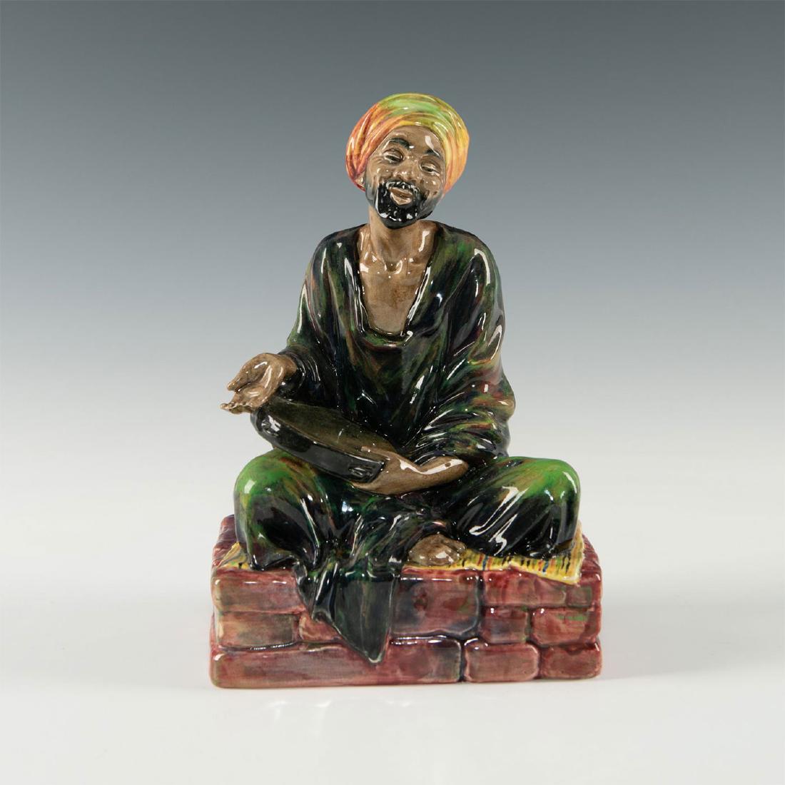 ROYAL DOULTON FIGURINE, THE MENDICANT HN1365: Modeled as a street beggar holding a tambourine. A glazed figurine in a green, purple and tan colorway, depicting a street beggar from a Middle Eastern bazaar, holding a tambourine to draw attention f