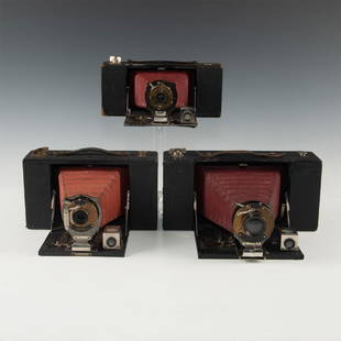 TRIO OF RARE RED LEATHER ANTIQUE FOLDING FILM CAMERAS: A "Goldilocks" sized array of Kodak Brownies, decked in brass. Issued: 1900s Dimensions: 10"L x 8.5"D x 5"H, largest, open Manufacturer: Kodak Country of Origin: United States