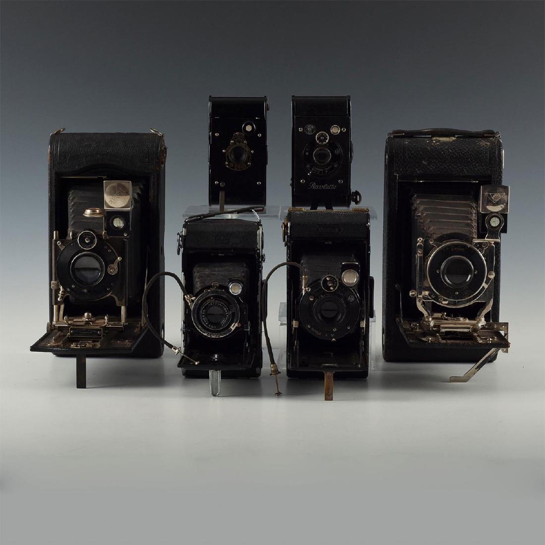 LOT OF 6 ANTIQUE FOLDING FILM CAMERAS PAIRED IN 3 SIZES: Ideal bookend or mantlepiece pairs of classic bellows cameras. Includes Kodaks, a Bionic, two Zeiss Ikons and a Contessa Piccolette. Both Zeiss cameras include cable remotes to complete the look. Issu