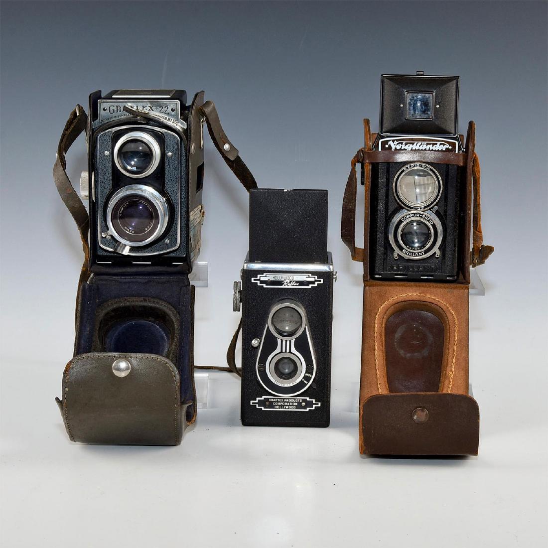 GROUP OF 3 ART DECO TWIN LENS REFLEX CAMERAS: Graflex TLR, Hollywood Reflex TLR, and a Voigtlanderï¿½TLR. Two with leather cases. Medium format roll film cameras includes a German Voigtlander, aï¿½Graflexï¿½model 22 with leather case and