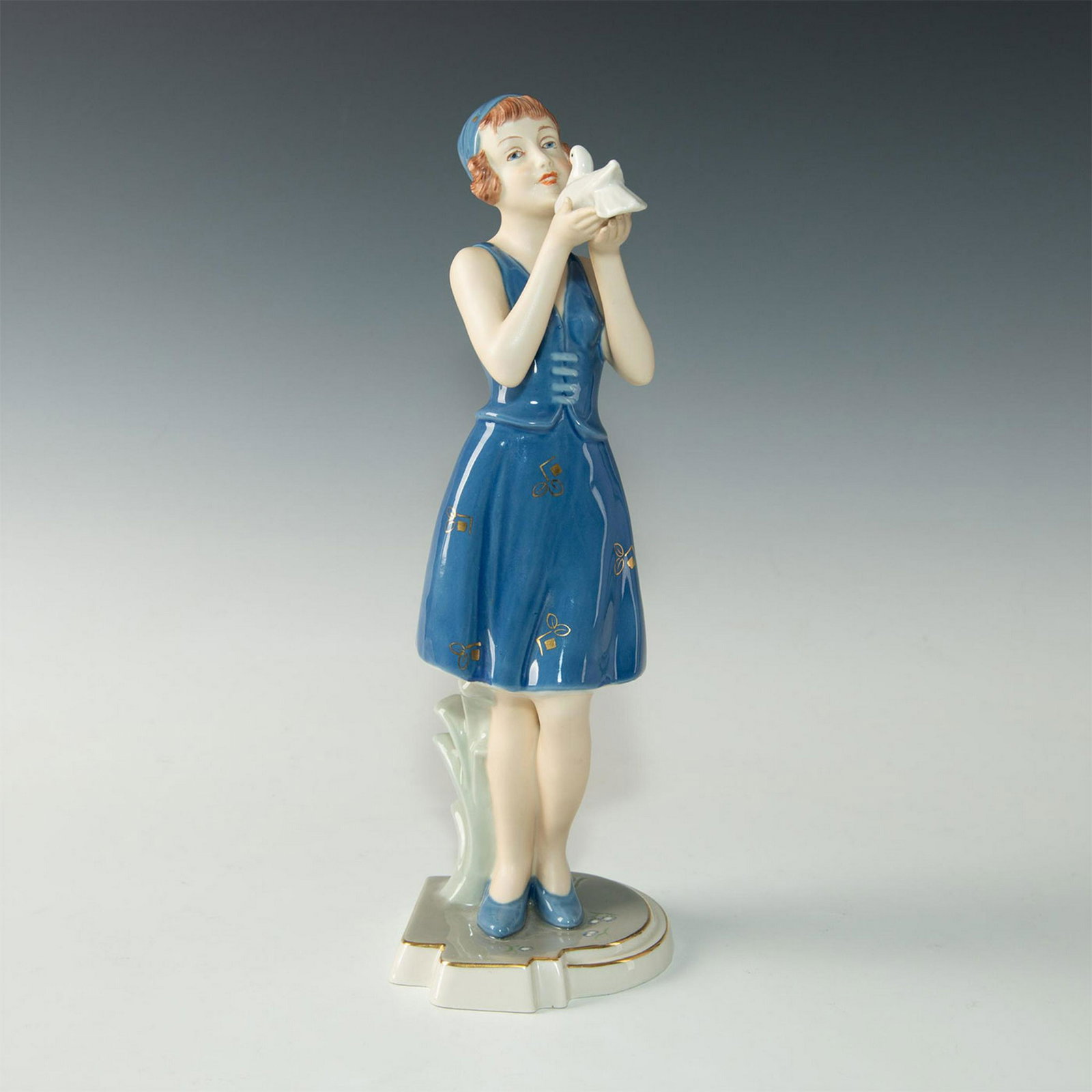 ROYAL DUX BOHEMIA ART DECO FIGURINE, WOMAN AND BIRD: Signed to base by Art Deco porcelain artist Schaff. A modernist early 20th century figurine of a young woman holding a white bird in her outstretched hands. Blue hat and dress with gilt decorative des