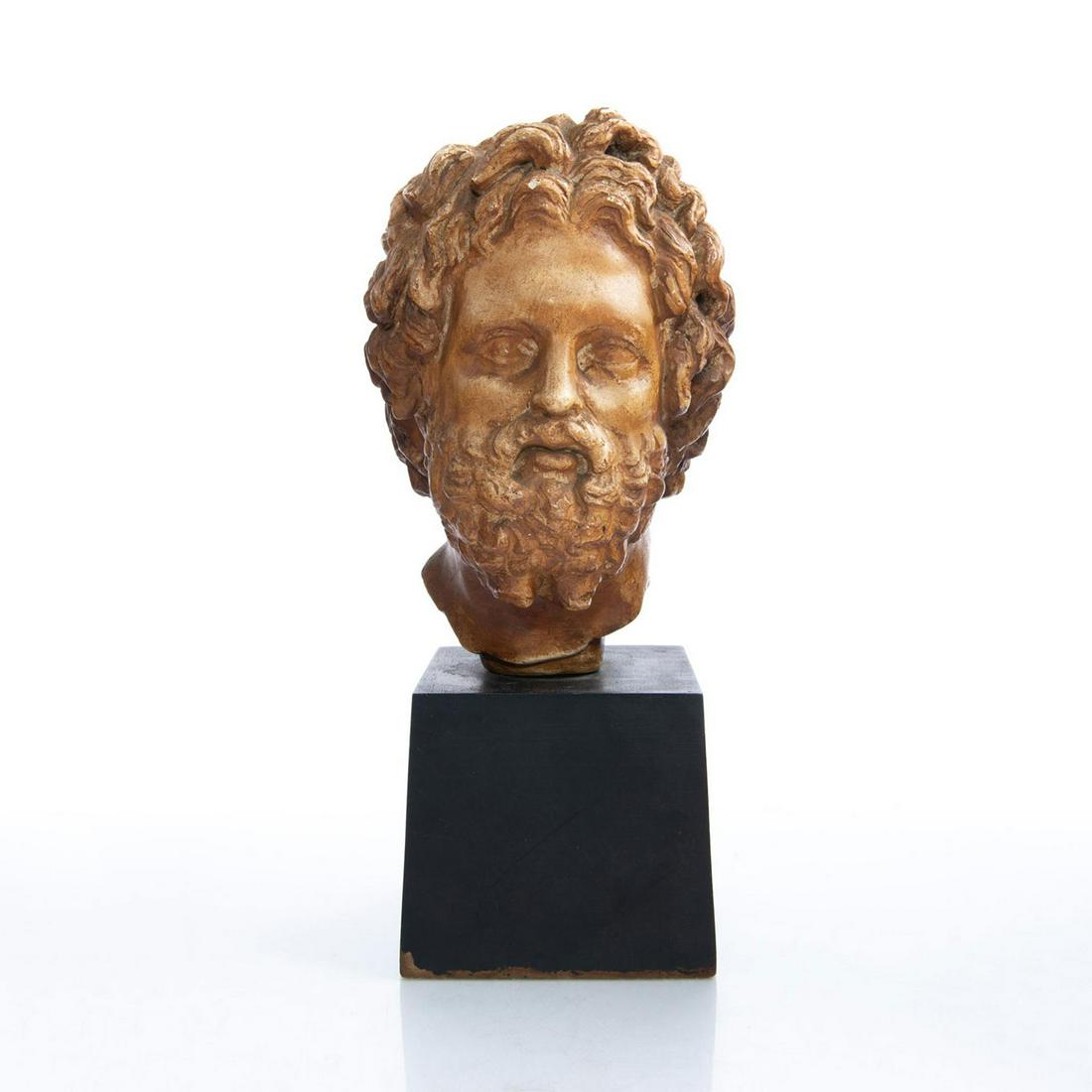 ALVA STUDIOS SCULPTURAL BUST, AFTER ASCLEPIUS OF MILOS: Neoclassical styled patinated plaster, presented on a black base. A museum reproduction of the monumental bust of Asklepios (Asclepius), Greek God of Healing. The original upon which it is based, the 