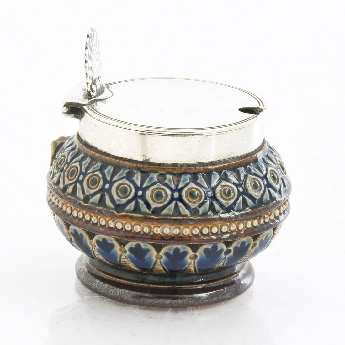 DOULTON LAMBETH LIDDED SALT CELLAR: Stoneware with silver lid. Geometric pattern body with silver shell lid. Silver is hallmarked on the side. Issued: 1880 Dimensions: 2.5"H Manufacturer: Doulton Lambeth, Hukin & Heath Country of Origin
