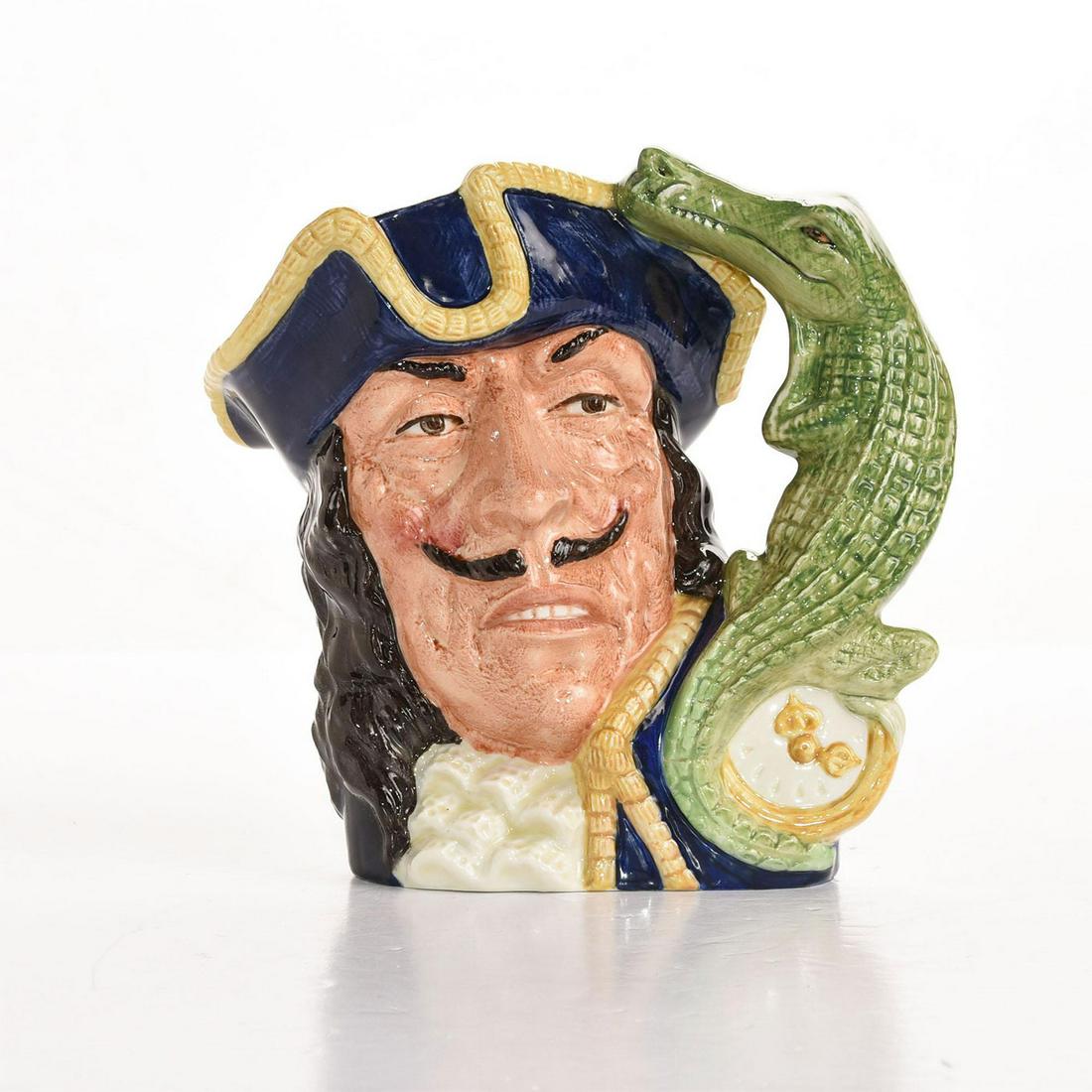 ROYAL DOULTON LARGE CHARACTER JUG, CAPT. HOOK: Crocodile and clock handle. Blue, yellow and green colorway. Captain Hook is the nemesis of Peter Pan in J.M. Barrie's story. Artist: David B. Biggs Issued: 1965-1971 Dimensions: 7"H Manufacturer: Roy