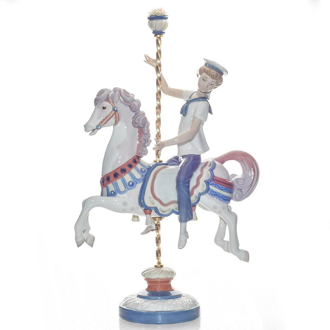 LARGE LLADRO FIGURINE, BOY ON CAROUSEL HORSE 01001470: Features sailor boy at a fair. Fine porcelain; glazed finish. Blue, white and green colorway. Item number inscribed in base. Includes original box. Artist: Jose Puche Issued: 1985-2000 Dimensions: 15"