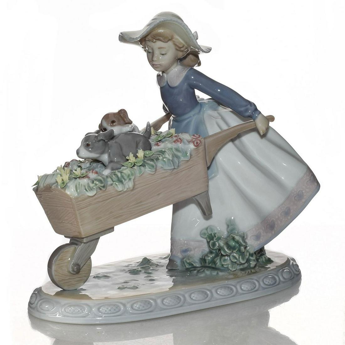 LLADRO FIGURINE, A BARROW OF FUN 01005460: Glazed porcelain; hand painted. Girl pushing dogs in barrow. Lladro stamp on the underside. Artist: Regino Torrijos Issued: 1988 Dimensions: 8.25"H Manufacturer: Lladro Country of Origin: Spain