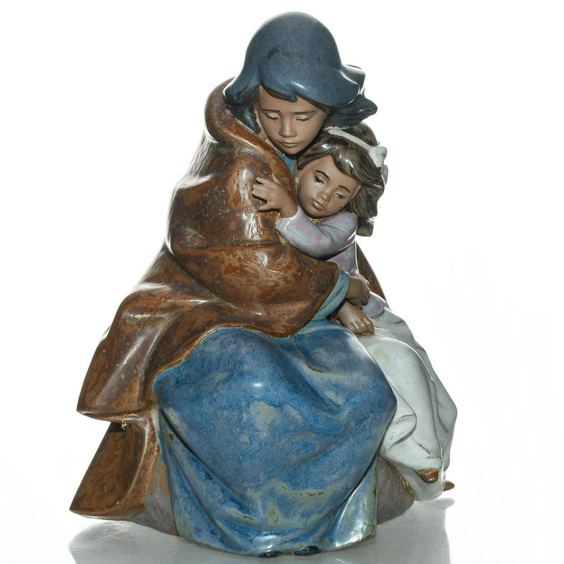 LLADRO FIGURINE, SISTERLY LOVE 0102206: Depicts sisters hugging, comforting each other. Stoneware; gres. Blue and ochre tones. Lladro backstamp. Complete with box. Artist: Jose Puche Issued: 1990-2002 Dimensions: 9.5"H Manufacturer: Lladro 