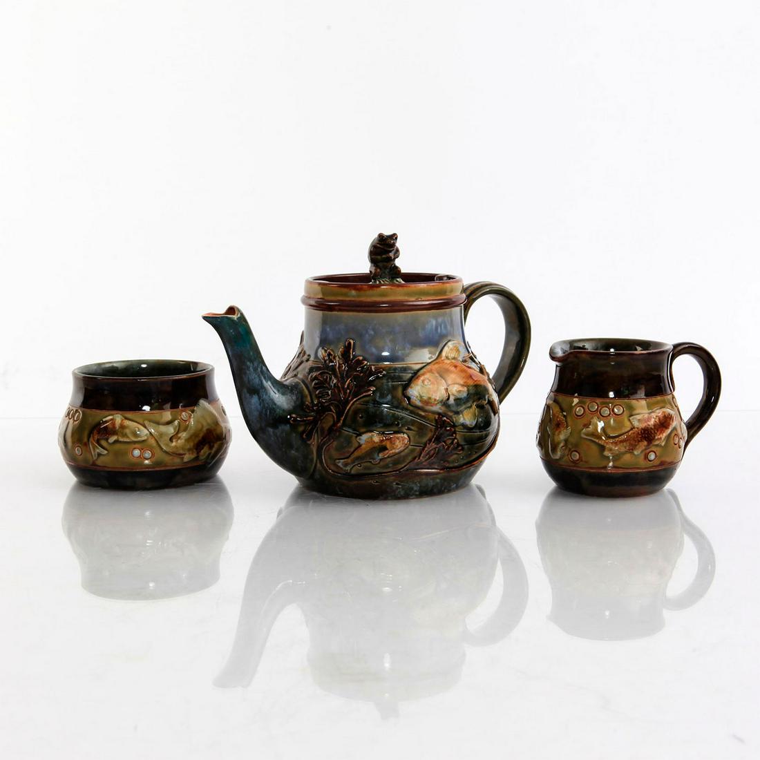 GEORGE TINWORTH DOULTON LAMBETH TEA SET: Includes teapot with frog finial to lid, sugar bowl and creamer. Designed by George Tinworth with relief fish designs. Impressed Royal Doulton England to base with artist marks. Artist: George Tinwort