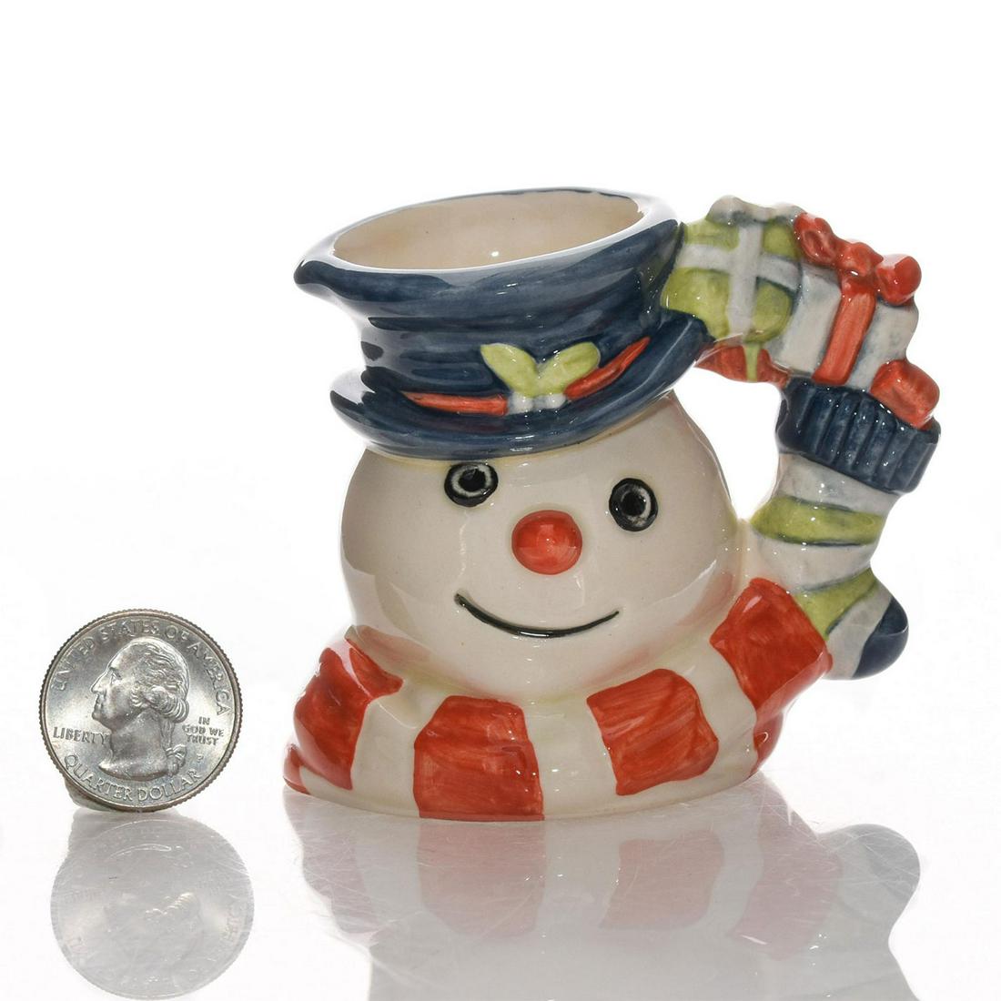 SNOWMAN D7124 - MINI - ROYAL DOULTON CHARACTER JUG: Mini character jug of smiling snowman with blue hat and scarf. The handle features Christmas presents and a stocking. Issued: 1998 Dimensions: 3"H Manufacturer: Royal Doulton Country of Origin: Englan