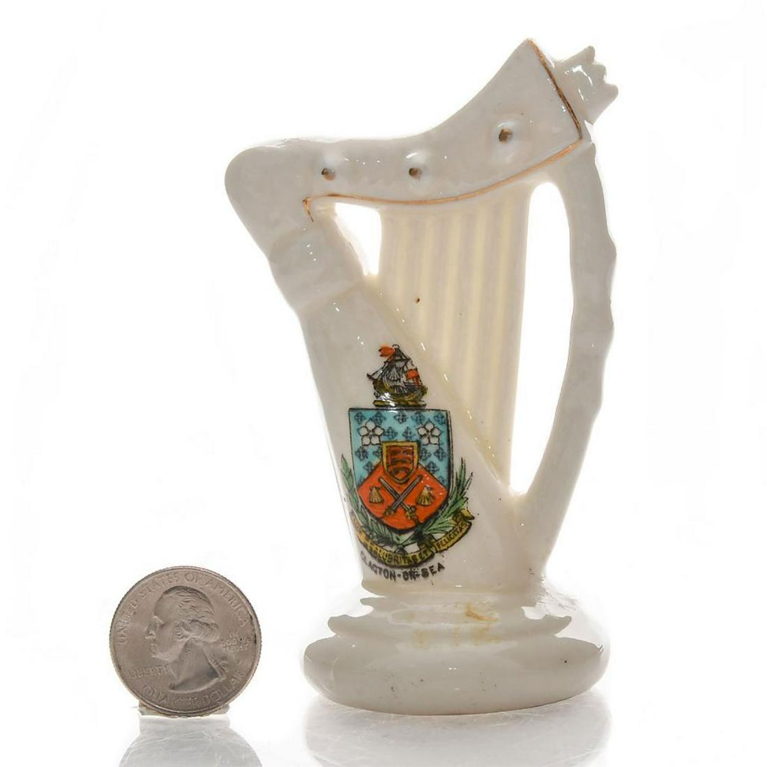 ARCADIAN CRESTED HERALDIC CHINA HARP, CLACTON-ON-SEA: Glazed white china harp with hand painted and gilt accents. Clacton on Sea coat of arms on front. Arcadian stamp on bottom. Dimensions: 4"H Manufacturer: Arcadian Country of Origin: England