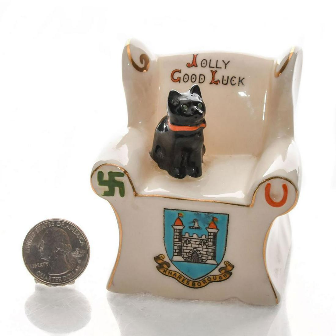 CARLTON CRESTED HERALDIC CHAIR WITH CAT, KNARESBOROUGH: Glazed white china chair with cat and gilt decoration. Knaresborough crest on front. Black on seat. Carlton China stamp on bottom. Dimensions: 3"H Manufacturer: Carlton China Country of Origin: Englan