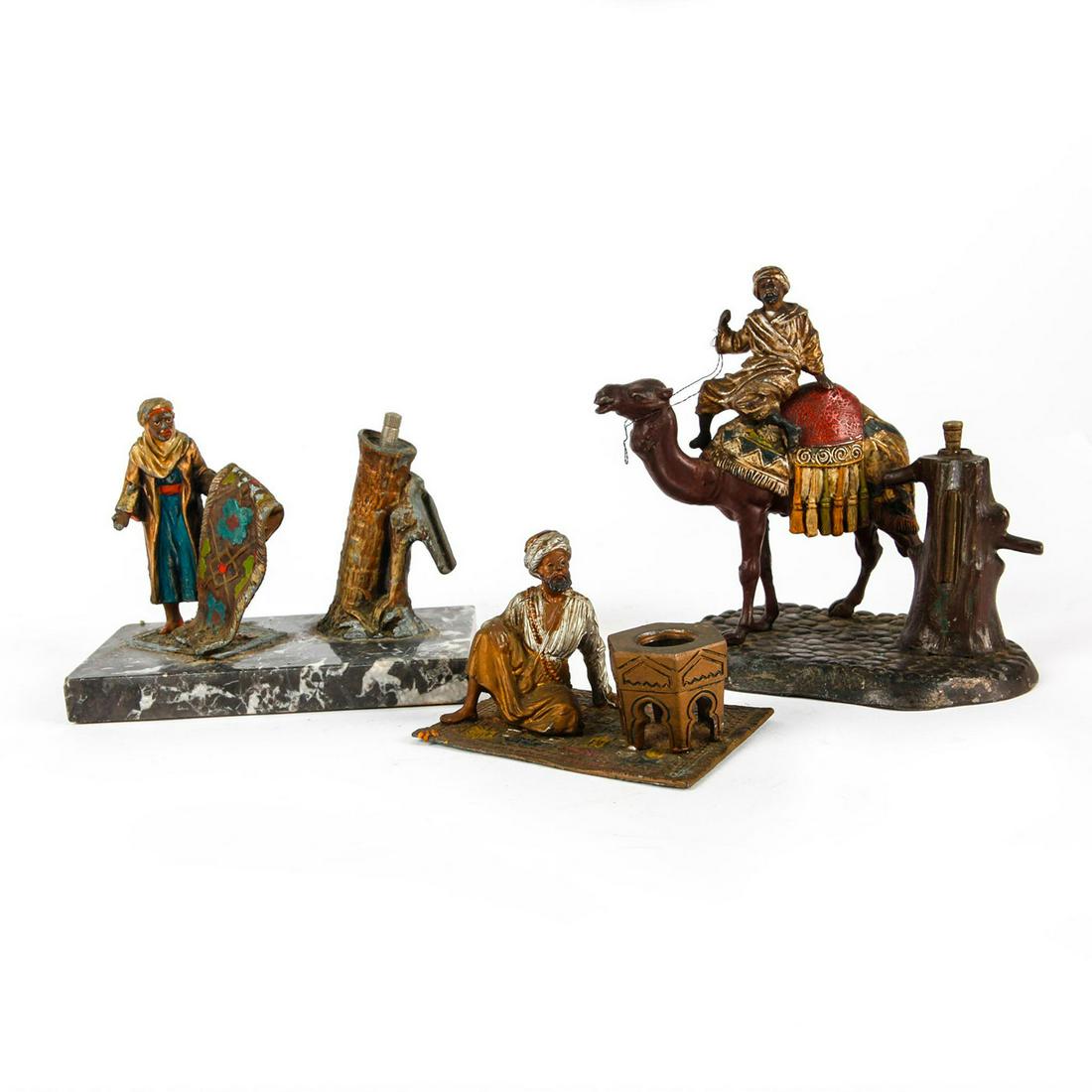 THREE AFRICAN MOORISH METAL PAINTED FIGURES: Man on camel, man holding carpet and man sitting on carpet. Varying patina on all. The figural with man on camel (6.5"H) and man holding carpet (5"H) both include a water pump. The man holding carpet 