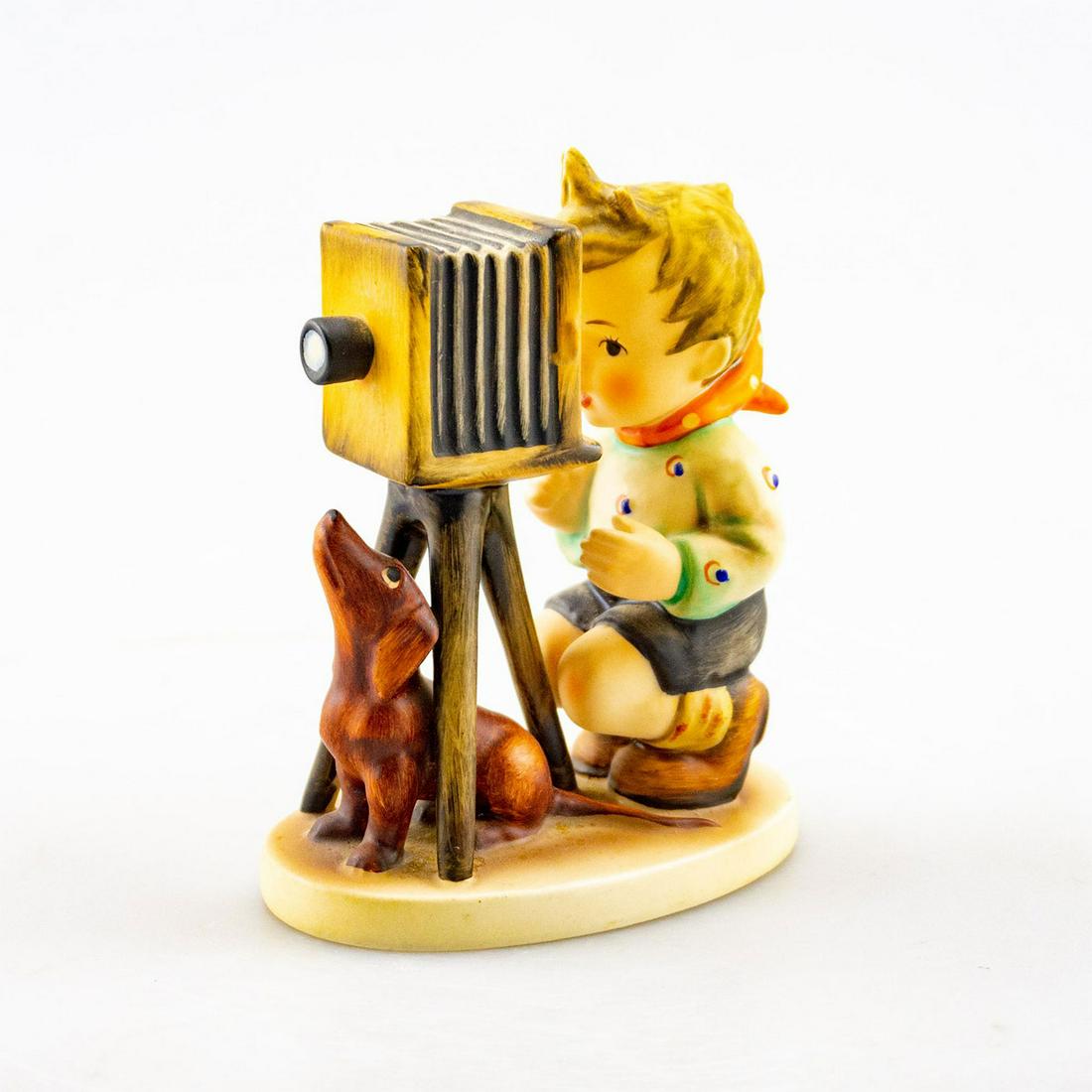 GOEBEL HUMMEL FIGURINE, THE PHOTOGRAPHER 178: A boy looks through his camera with his dog next to him. Artist: Goebel Issued: 20th c. Dimensions: 5"H Manufacturer: Goebel Country of Origin: Germany