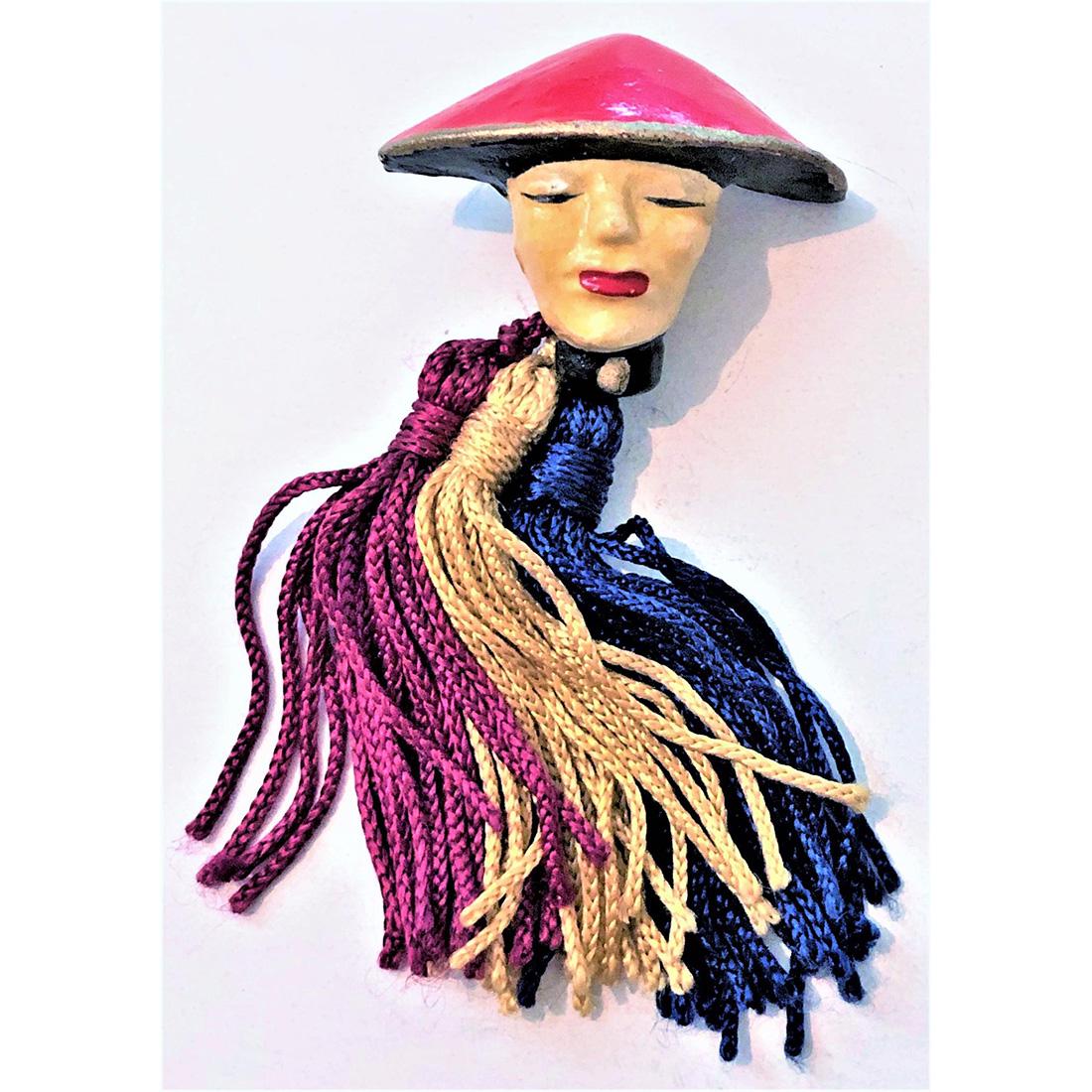 A SCARCE 1930: 1 large Asian head of plaster with fabric tassels by Schiaparelli. The tassels match the paint colors of red, blue and yellow used on the plaster head. Elsa Schiaparelli was considered one of the most
