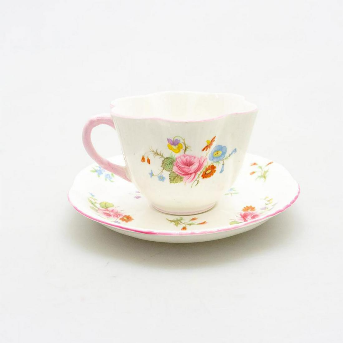 SHELLEY BONE CHINA TEACUP AND SAUCER, ROSE & RED DAISY: A traditional English bone china cup and saucer, with pink, red, yellow, and green flora. Glazed cream with profuse multicolored flowers, and pink trim. Hairline crack to tea cup. SHELLEY FINE BONE CH