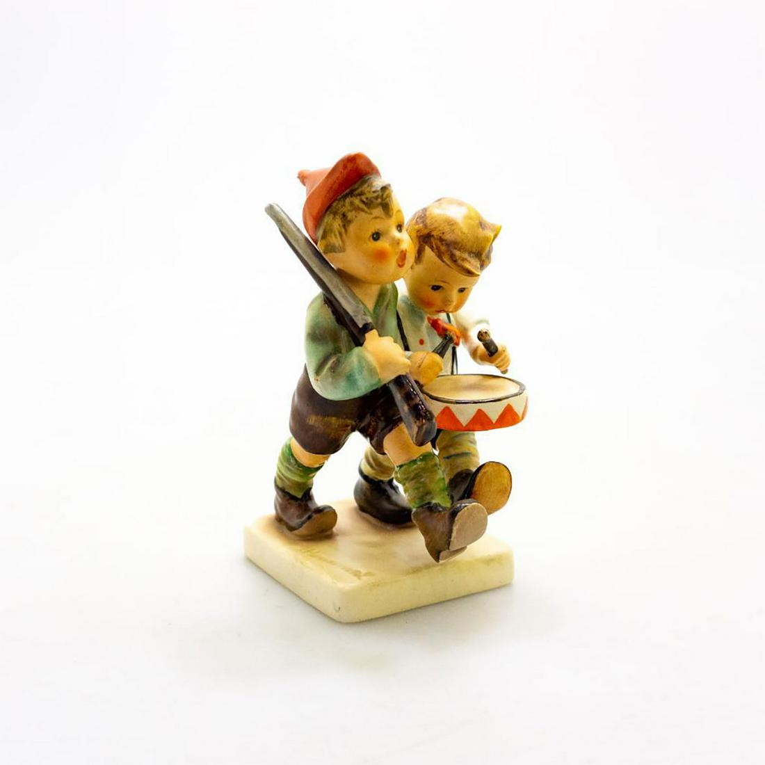 Goebel Hummel Figurine, Volunteers 50: Ceramic; hand painted. Goebel backstamp. Chip to young boy's leg. Issued: 20th c. Dimensions: 5.5"H Manufacturer: Goebel Country of Origin: Germany