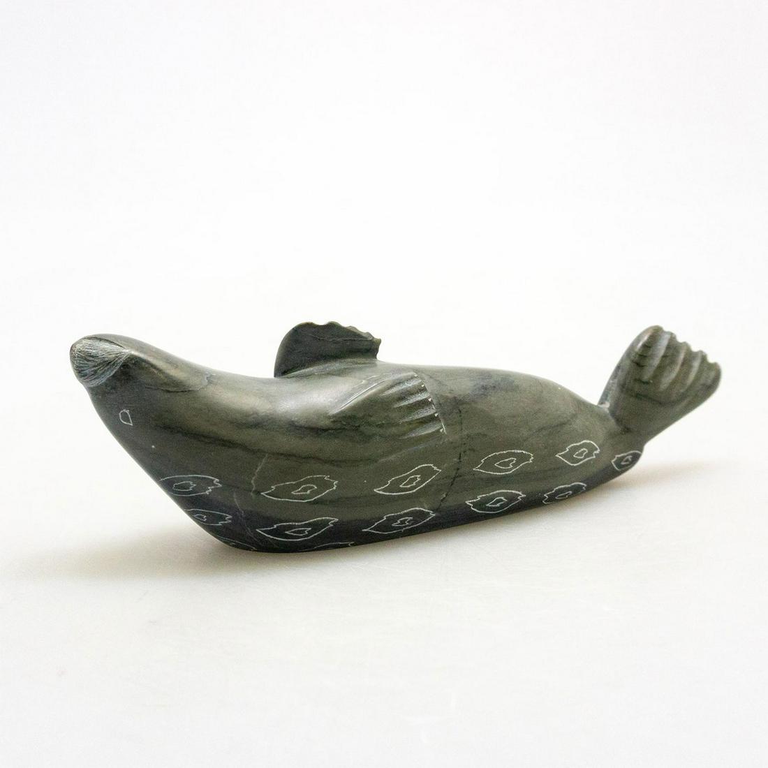 Inuit Tribal Soapstone/Regional Stone Figurine: A dark gray hand carved stone sea lion seal, incised details. Artist signed. This Inuit soapstone carving is modeled as a playful arctic seal, swimming on its back. Modeled in dark gray stone with inc