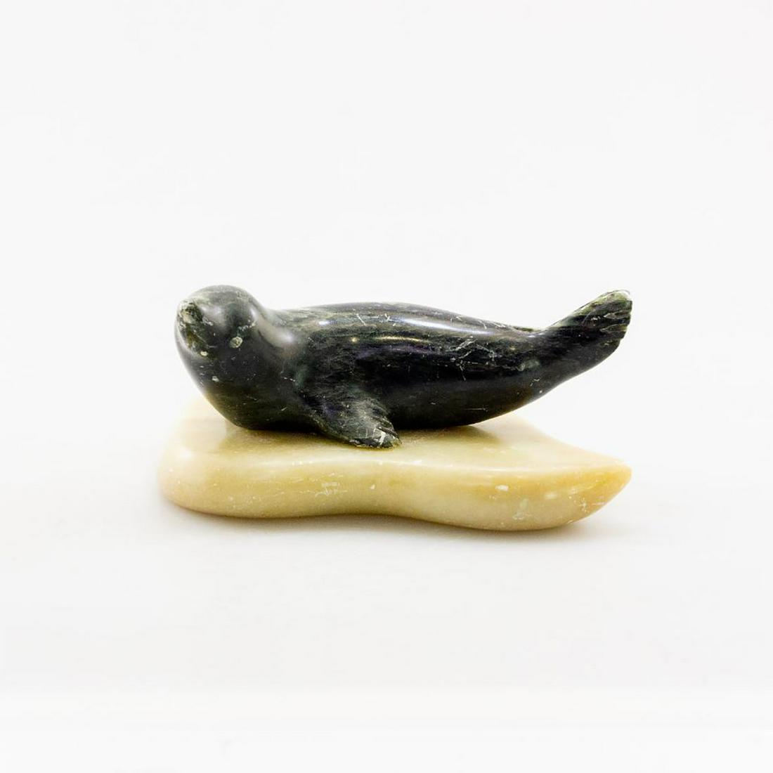 Native Alaskan Eskimo Sculpture, Seal On An Ice Floe: Artist signed, black and cream soapstone/regional stone with inclusions. Hand carved in a naturalistic style, a seal reclines on the ice. Black stone with gray and white inclusions on cream soapstone.