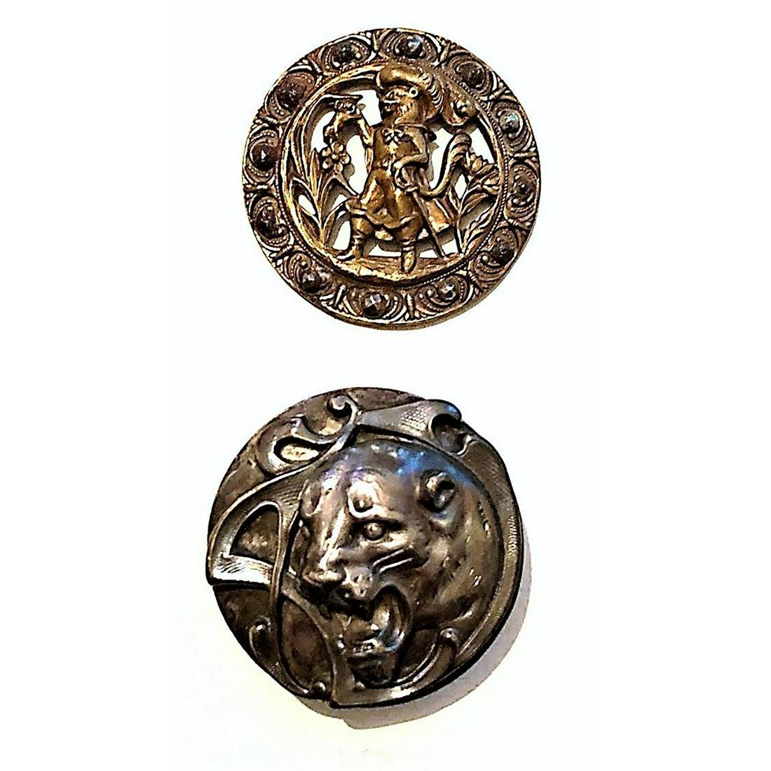 A Pair Of Division 1 Metal Cat Family Buttons: 2 Large brass and silvered metal buttons depicting Cats. The brass example is a peered depiction of "Puss N Boots" and a cut steel border, and the silvered example is an incredibly detailed high relie