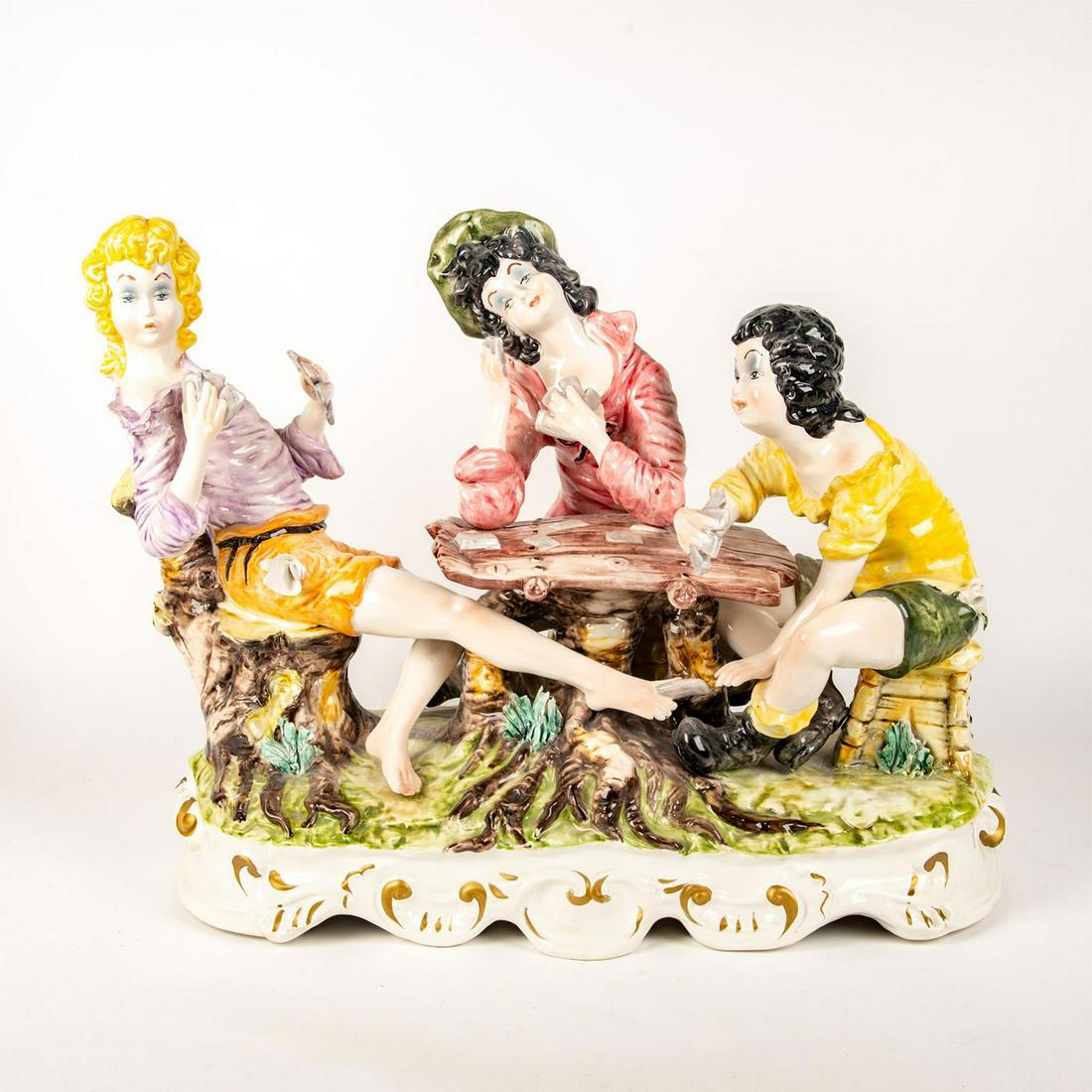 Large Hand Painted Porcelain Figurine Grouping, The: Style of Capodiomonte, modeled as 3 ladies playing cards with 2 cheating, on Rococo style base. Maker's mark to bottom base. Small chips throughout. Issued: 20th c. Dimensions: 28"L x 19.25"H