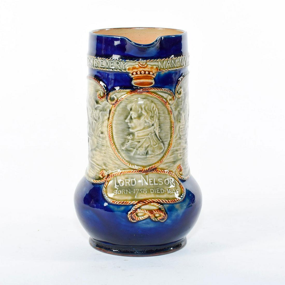 Royal Doulton Stoneware Pitcher, Lord Nelson: Men of History; Commemorates Nelson's victory at the Battle of Trafalgar. Features portrait of Lord Nelson and scene of ships at sea encircling body. Cobalt blue and green glaze; brown twisted rope ha