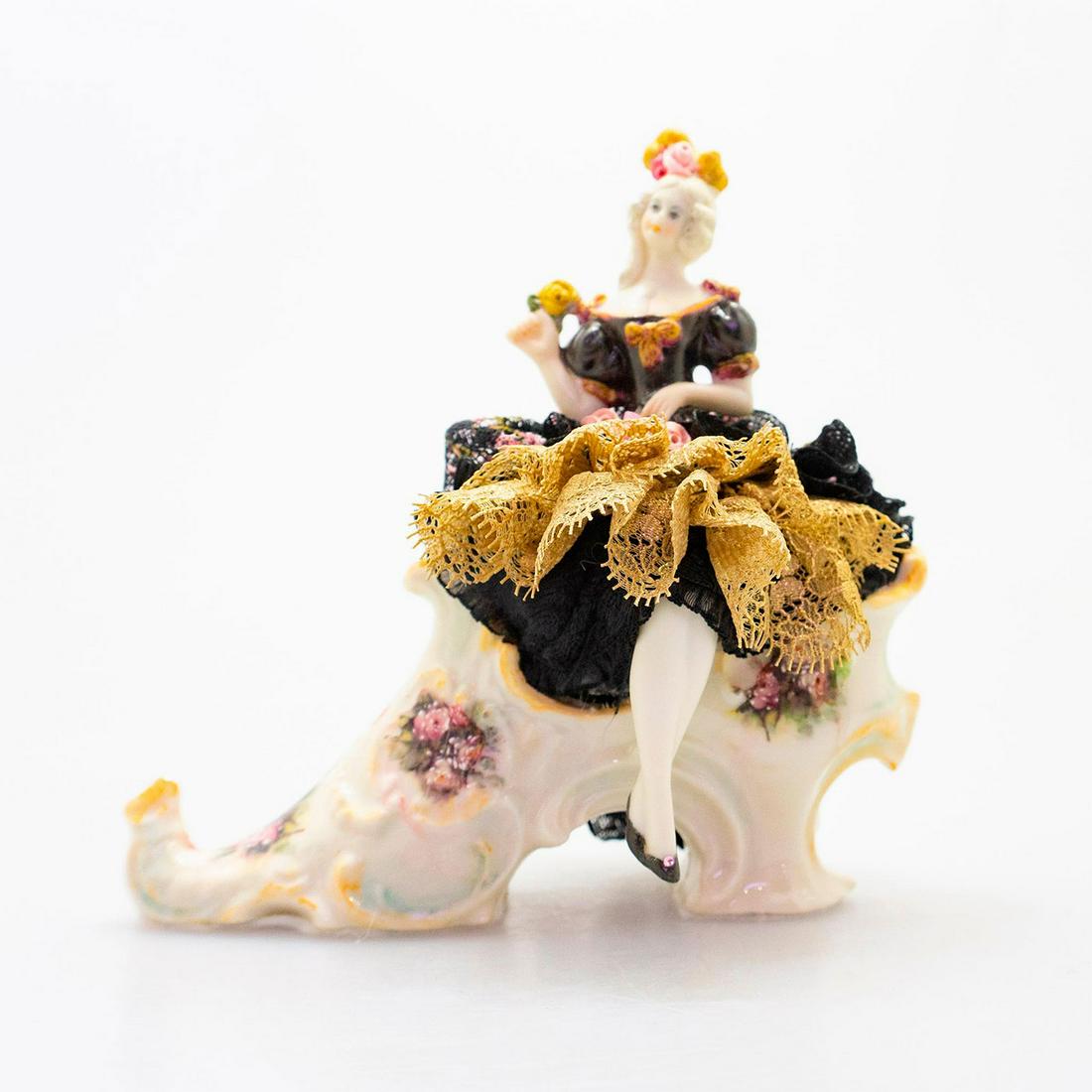 Vintage Collectible Figurine, Woman In Shoe: German style half doll figure seated in porcelain high heel shoe; fabric lace dress. Black and gold dress; pink ribbon accents. Floral design on shoe. Unmarked. Issued: 20th c. Dimensions: 6"H
