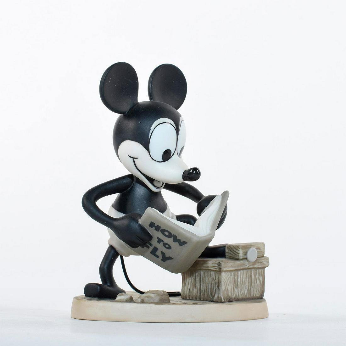 Disney Classics Figurine, Mickey Mouse, Plane Crazy: Mickey stands with one leg propped up reading his 'How to Fly' manual. Black and white ceramic figure of Mickey Mouse from the 1928 Disney film 'Plane Crazy'. Bottom stamp reads 'Mickey's 70th Birthda