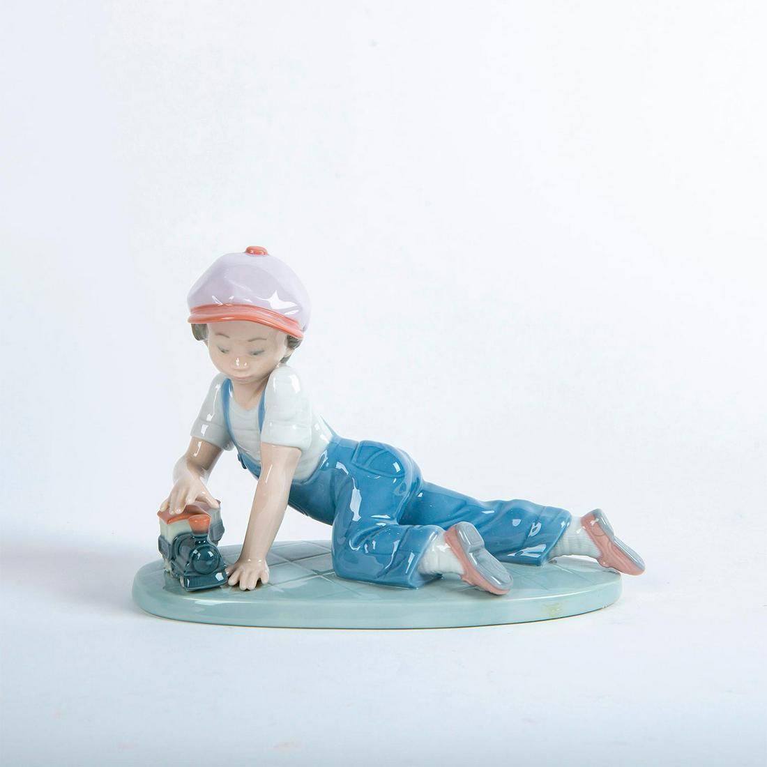 Lladro Porcelain Figurine, All Aboard 01007619: Glossy porcelain figurine of a little boy playing with a toy train. Lladro backstamp. Does not include original box. Artist: Antonio Ramos Issued: 1992 Dimensions: 5"H Country of Origin: Spain Manufac